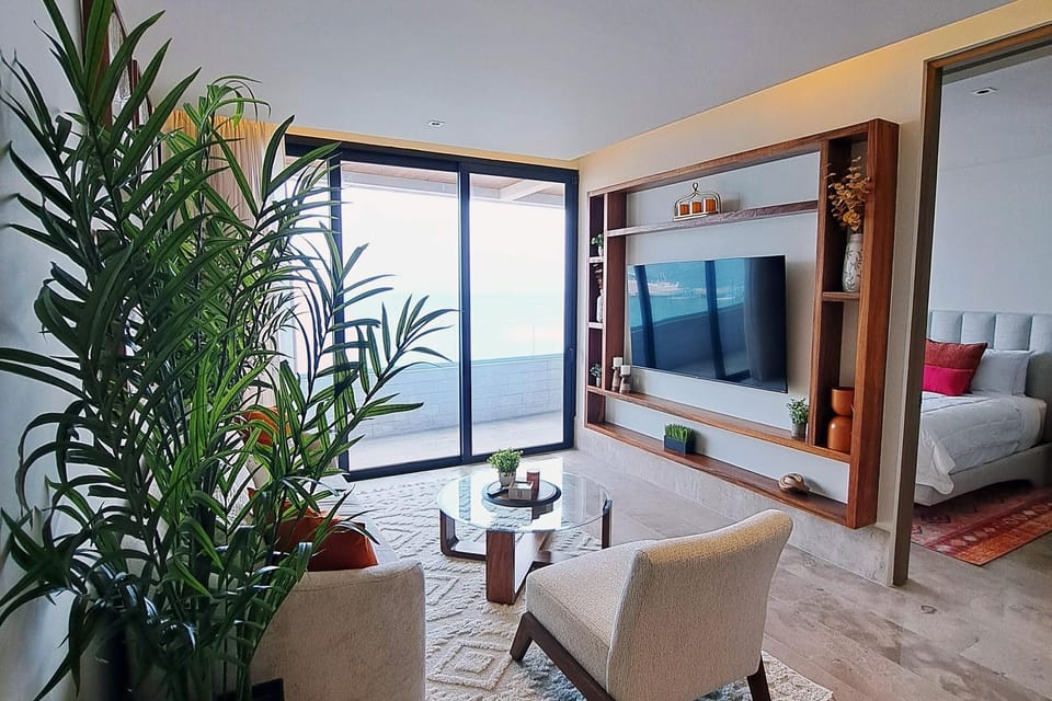 Living room with glass sliding doors overlooking the balcony, a round glass coffee table, and a built-in wooden TV frame.
