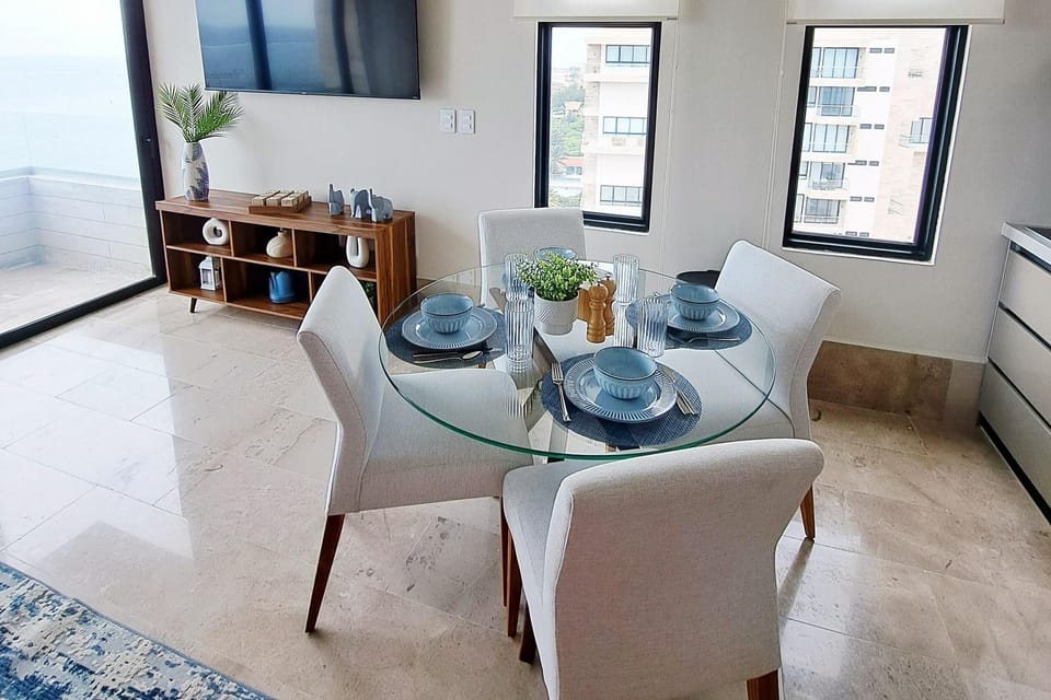 Round glass dining table set with blue dishware and white upholstered chairs on marble tile floor.