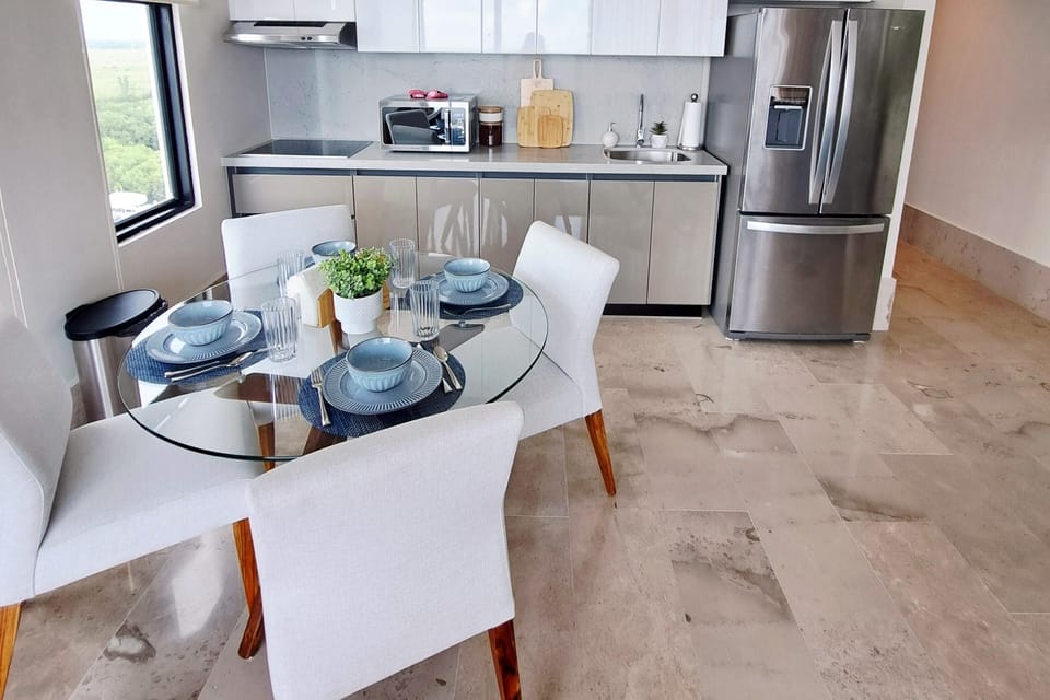 Glass-top dining table set with blue dishware and white cushioned chairs on polished stone tile.