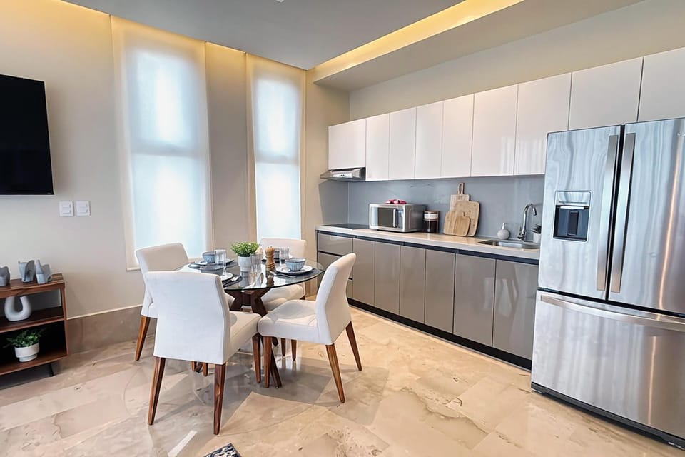 Kitchen and dining area with marble floors, gray and white cabinets, glass-top table, and stainless steel refrigerator.