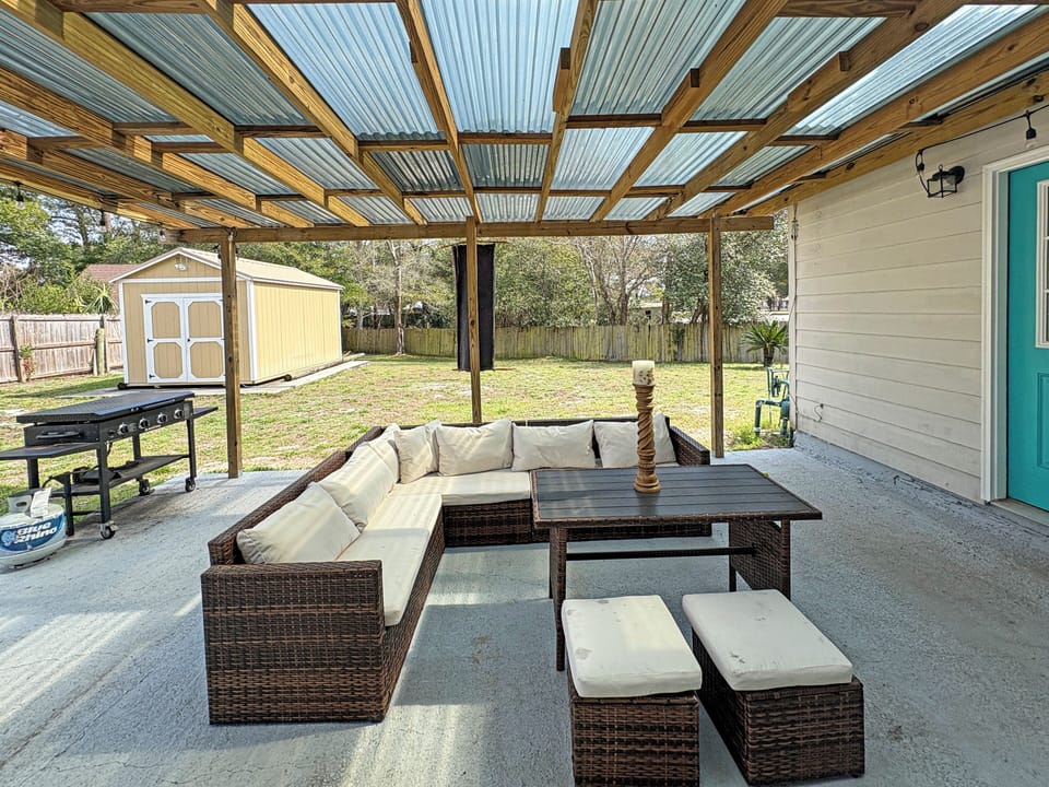 Covered backyard patio with lounge seating, grill, and fenced yard