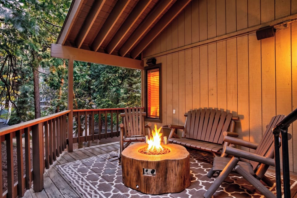 Covered forest-view deck with Adirondack seating and a cozy gas fire pit for relaxed evenings.