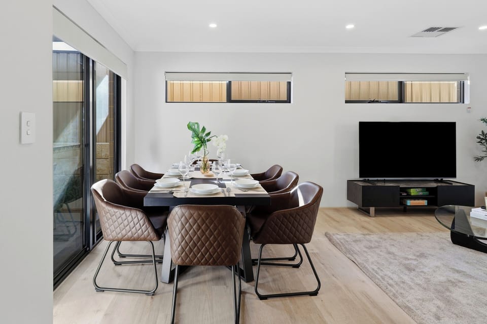 Enjoy the seamless flow of our open-plan home, featuring a grand dining table with quilted leather chairs for eight, a large smart TV, and sliding doors that open out to the patio area.