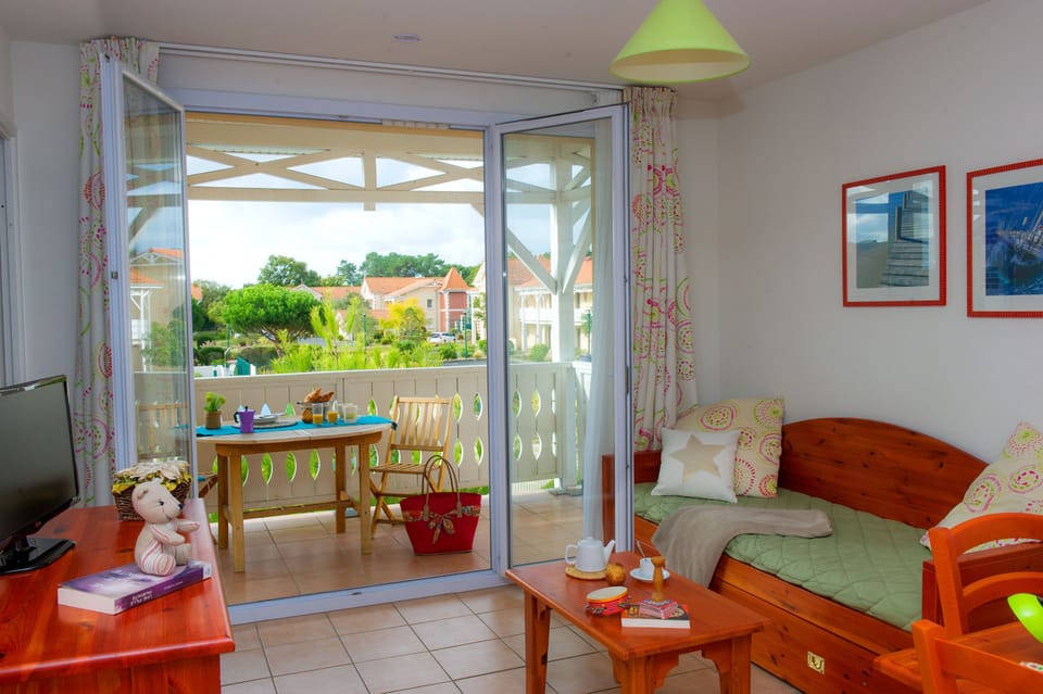 Living area with wooden daybed, green bedding, TV, and doors opening to the terrace.