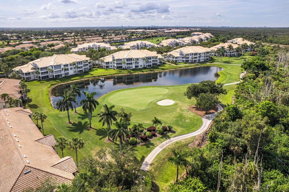 Aerial view of the resort community featuring multi-story residential buildings surrounding a pristine golf course with water features, tropical landscaping, and palm trees throughout the expansive grounds.