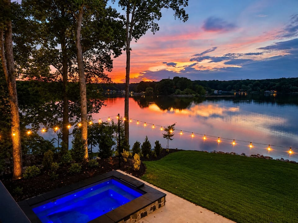 Lakefront sunset views with a glowing hot tub and dreamy string lights
