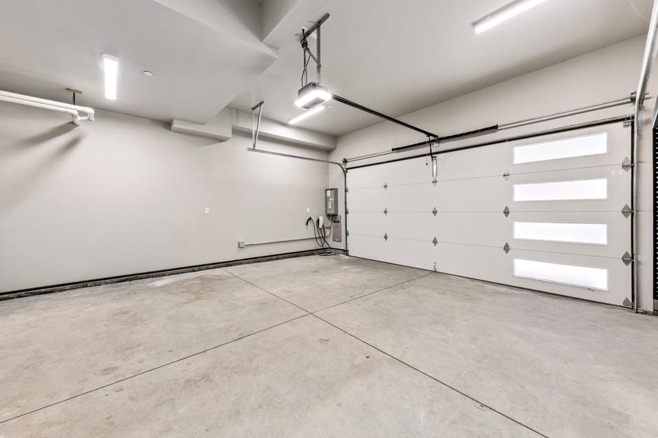 Two-car garage with smooth concrete floor, white walls, ceiling-mounted lights, and frosted window panels.