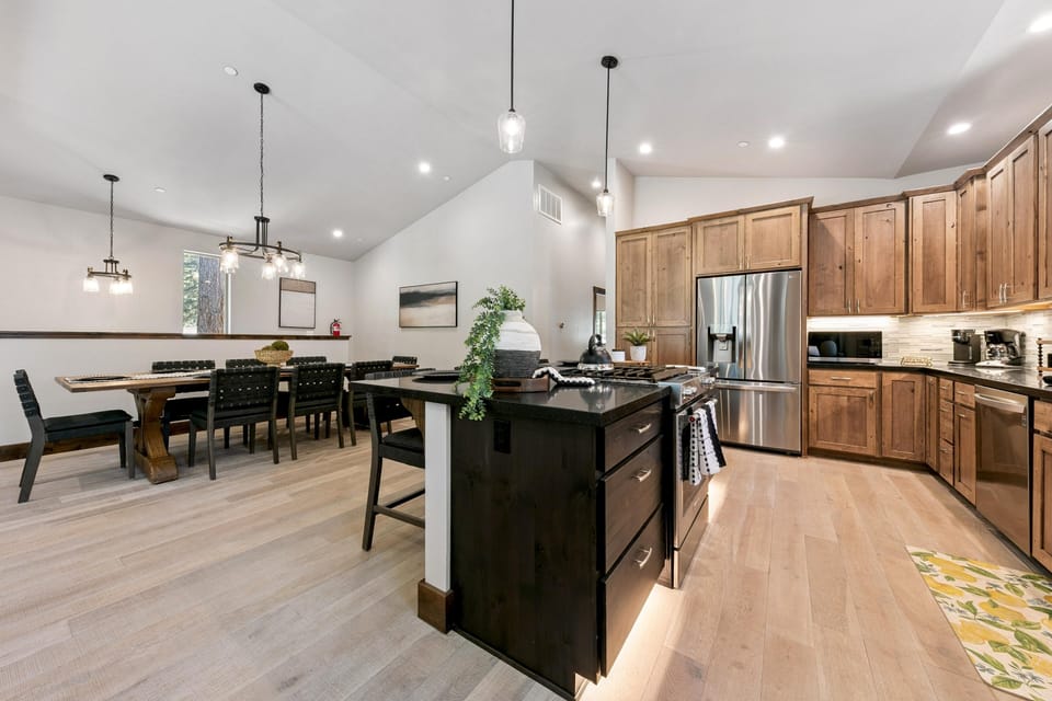 Kitchen and dining area with natural wood cabinets, black granite island, stainless steel appliances, and a large wood table.