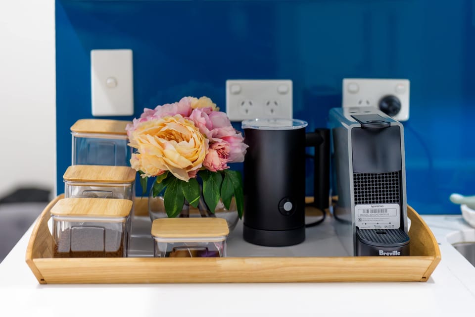 Coffee station with a Nespresso machine, milk frother, and stocked canisters, all set on a wooden tray. A fresh floral touch and clean styling make starting your morning simple and enjoyable. 