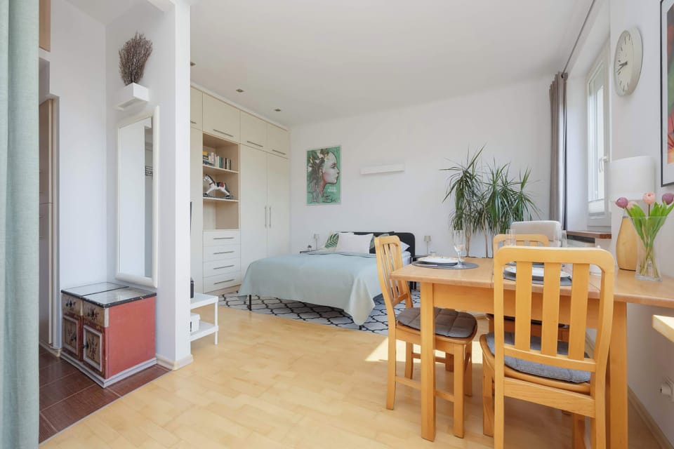 The studio is viewed toward the dining area and entrance, emphasizing the practical arrangement of furniture. Bright finishes create a welcoming interior.