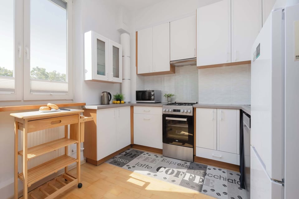 Another kitchen view highlights the L-shaped countertop, generous storage, and natural light from the nearby window. Modern appliances blend seamlessly with the cabinetry.