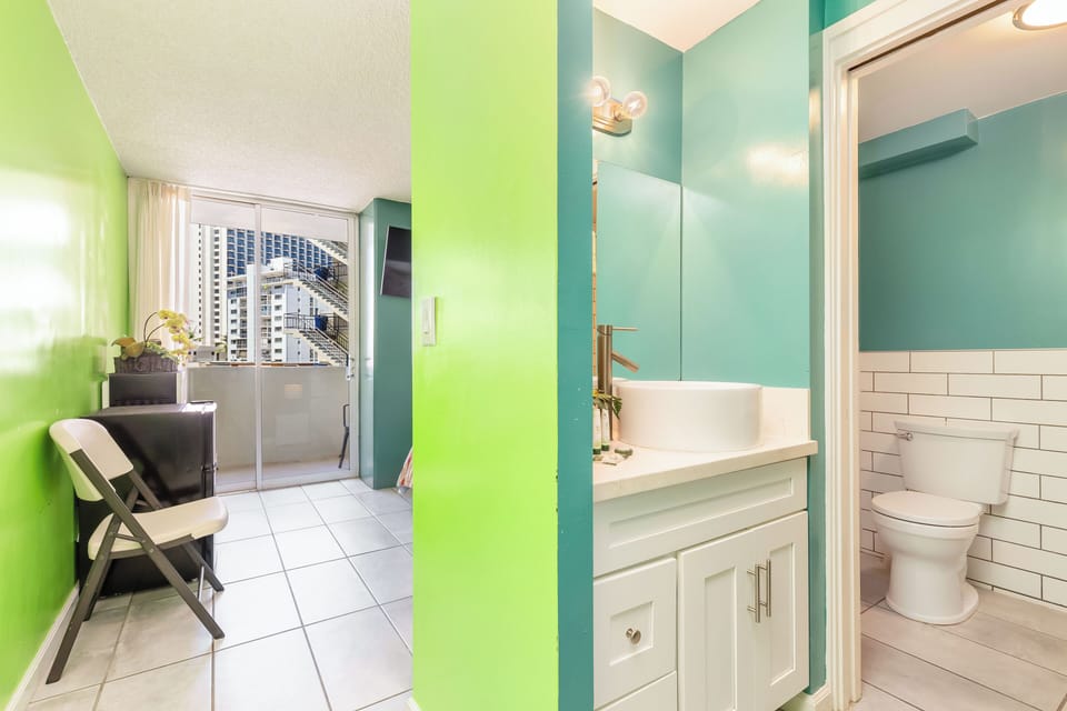 Modern bathroom with crisp white subway tile and a sleek vanity leads to a bright balcony with city views you can enjoy during your stay.