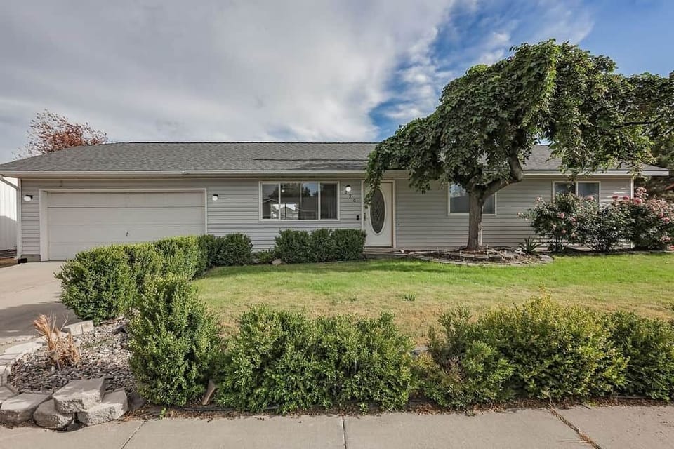 Welcoming front exterior with mature tree, landscaping, and easy driveway parking