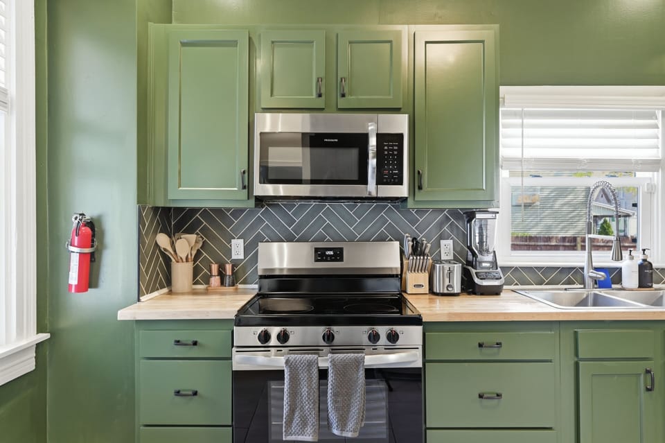 Chic green kitchen: stainless range, herringbone tile, fully stocked.