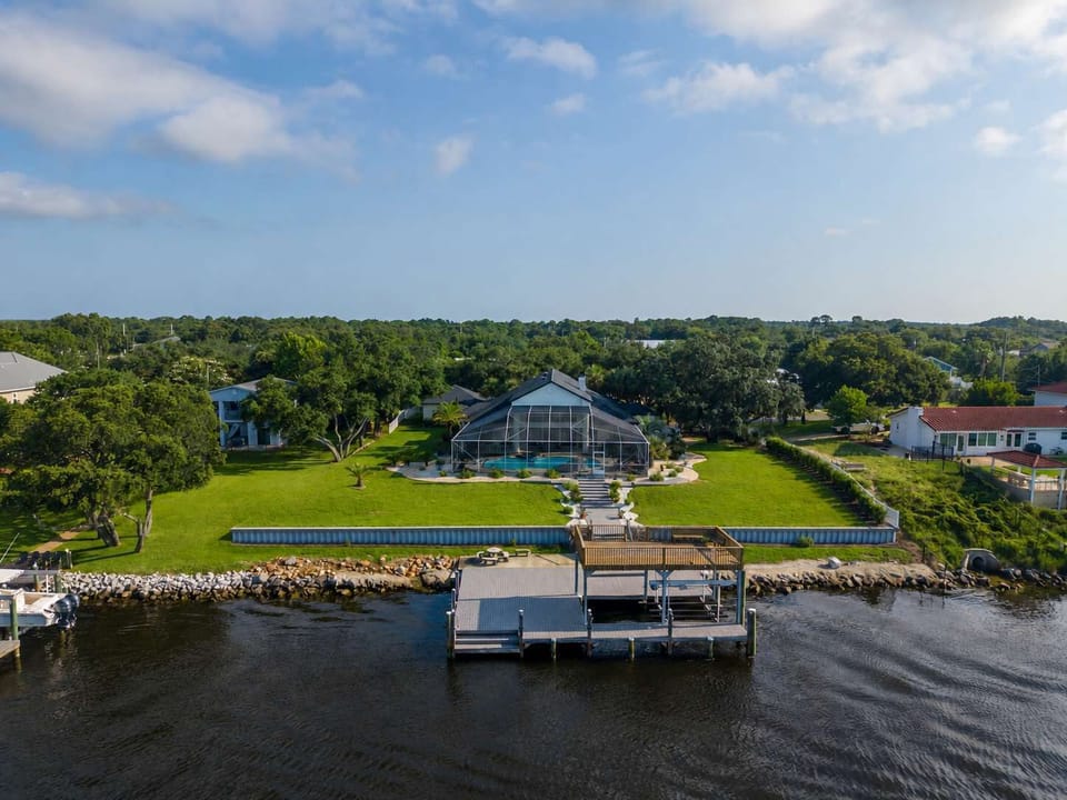 An aerial view captures this waterfront vacation rental in Innerarity Point, Perdido Key, showing the private dock, screened pool, and lush grounds toward the Intracoastal Waterway. Sleeps up to 15 guests.