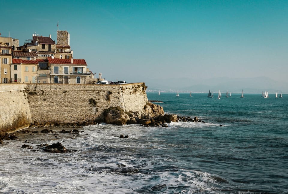 Medieval stone sea walls rising directly from the rocky Antibes shoreline with sailboats on open water