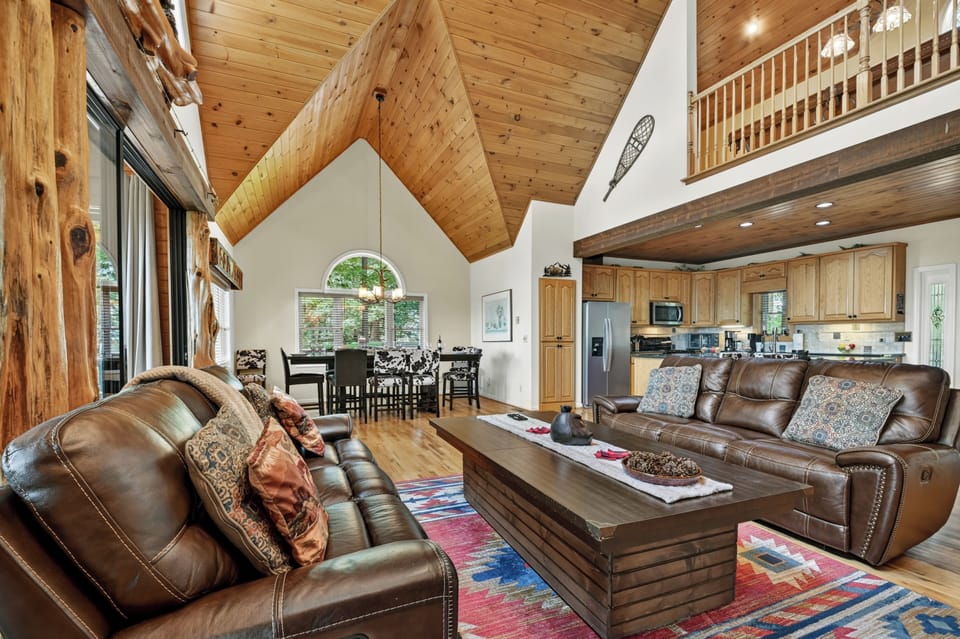 The spacious living area of this luxury cabin rental features soaring ceilings, a stunning stone fireplace, and plenty of comfortable seating