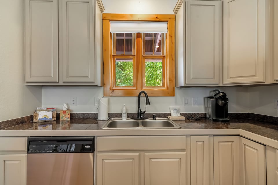 Whip up your morning coffee in this bright, well-equipped kitchen with granite counters, dishwasher, and a charming window overlooking lush greenery.