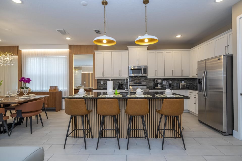 Kitchen island with black countertop, brown leather bar stools, white cabinetry, and stainless steel appliances.