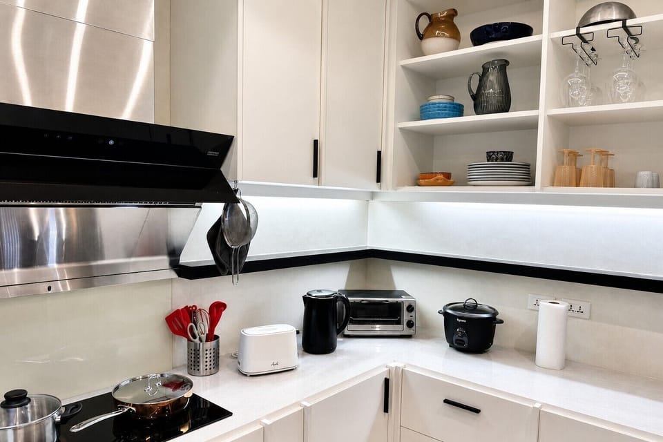 【Full Kitchen】An induction hob under a range hood, with a toaster, mini oven, electric kettle and rice cooker along the counter and glassware on the open shelves. Everything is included and ready to cook a full meal on arrival.