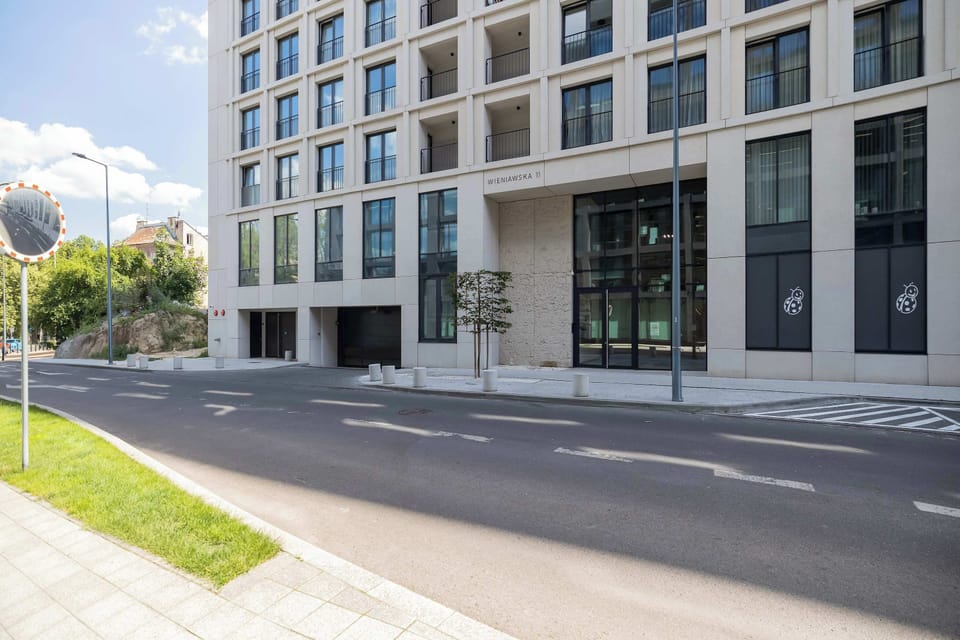 A modern residential building with well-maintained surroundings and wide walkways. The location offers easy access to the city center.