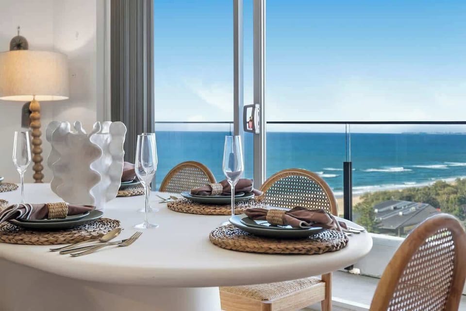 Oceanfront Dining Setup An elegantly styled table set with premium dinnerware and chic woven chairs. Overlooking breathtaking, uninterrupted ocean views, it provides a truly unforgettable backdrop for any vacation meal.