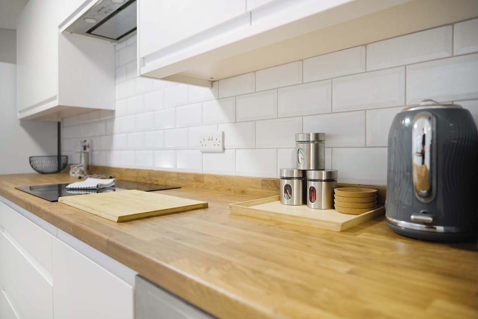 The kitchen features a fridge/freezer, oven, hob, sink, dishwasher, and storage space for utensils, cookware, and cleaning supplies. It also opens onto the backyard.