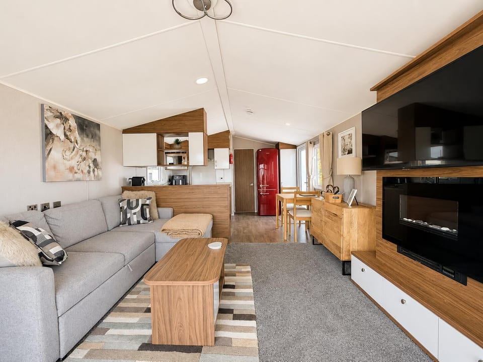 Open-plan living area with light grey sofa, wood coffee table, electric fireplace, and red retro fridge in kitchen corner.