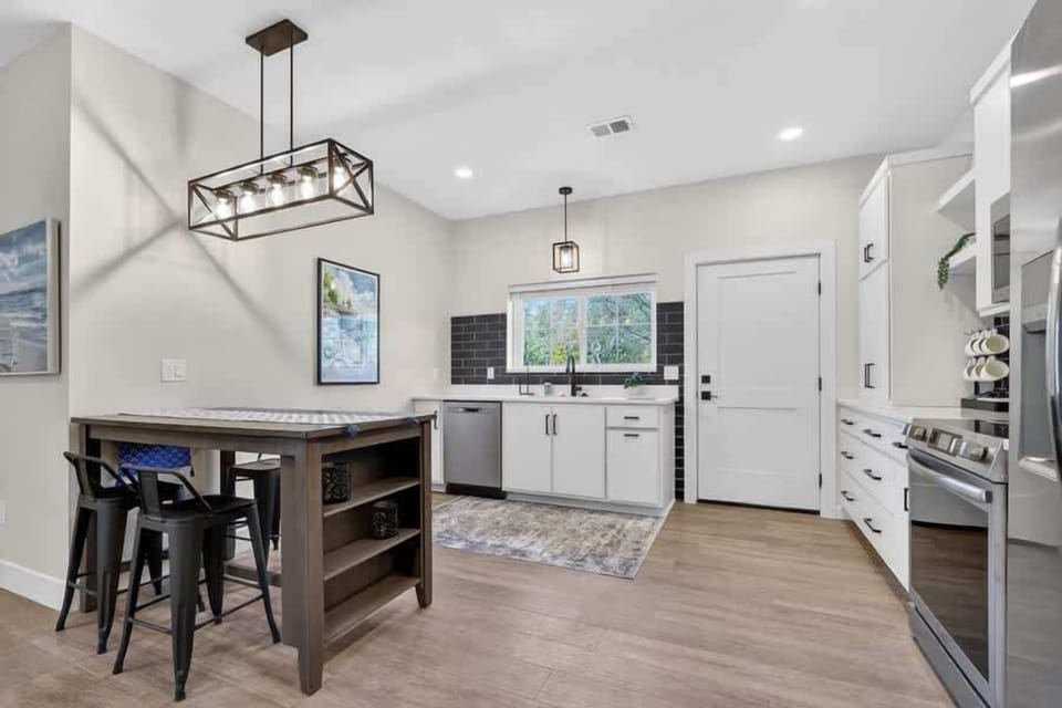Lower unit: your open-concept kitchen features modern white cabinetry, stainless steel appliances, and warm wood-tone flooring. The island with bar seating invites morning coffee or casual meals under elegant pendant lighting.