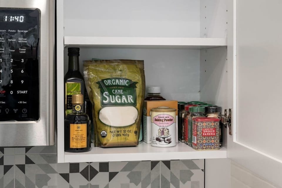 Kitchen pantry cabinet stocked with coffee, tea, sugar, honey, EVOO, balsamic vinegar, and spices. 
