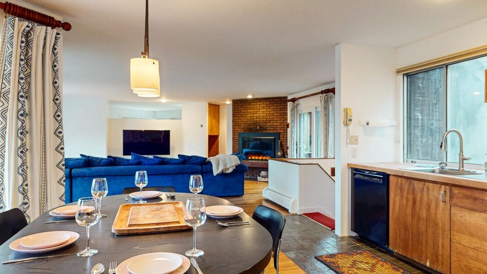 Enjoy effortless entertaining in this expansive open layout, featuring a dark wood dining table set for dinner with fine wine glasses.