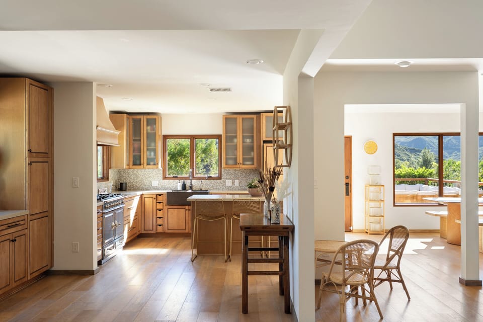 Bright kitchen and dining area with warm wood finishes and mountain views beyond the windows.