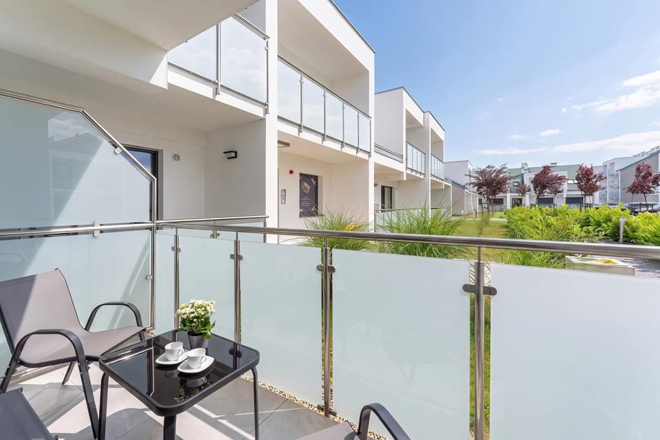The glass-enclosed balcony offers an unobstructed view of the beautifully landscaped community grounds. A small coffee table sits between two outdoor patio chairs.
