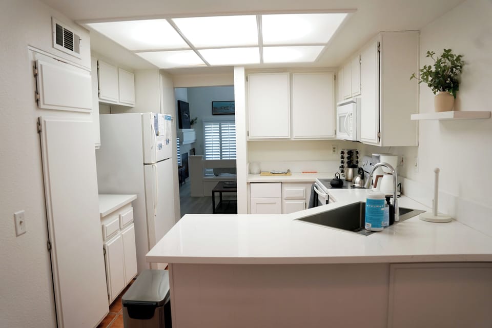 A clean, bright kitchen workspace featuring crisp white cabinetry, ample counter space, a convenient breakfast bar, and everything you need to whip up delicious meals.