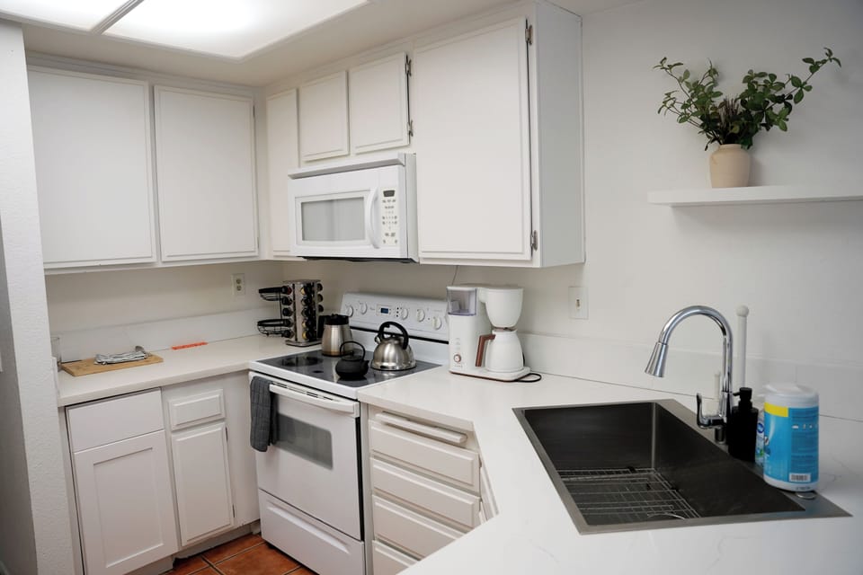 A closer look at your culinary space, featuring a deep stainless steel sink, sleek countertops, a full-size stove, an overhead microwave, and convenient coffee-making essentials