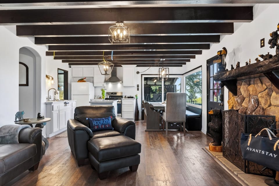 Open-concept living, dining, and kitchen area with rustic mountain charm, exposed wood beams, and scenic views through oversized windows.