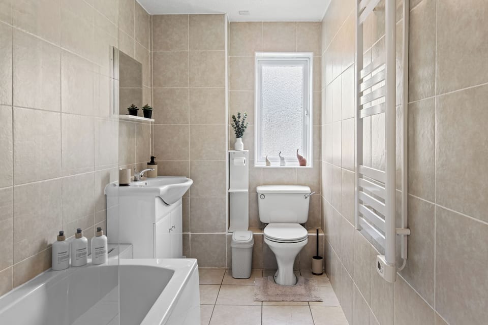 Bright tiled bathroom with tub, natural light, and heated towel rail