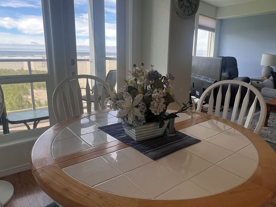 A charming circular dining table with a mirrored tiled top and elegant floral centerpiece creates an intimate spot for your meals, bathed in natural light from the nearby windows.