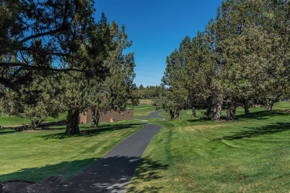 The property is set within a beautifully maintained golf course community, surrounded by mature trees and rolling green fairways under clear blue skies.