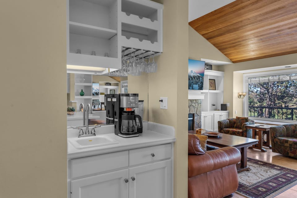 Your private coffee bar awaits with a wine glass rack and sleek appliances, seamlessly connecting to a sun-soaked living room with stunning views through expansive windows.