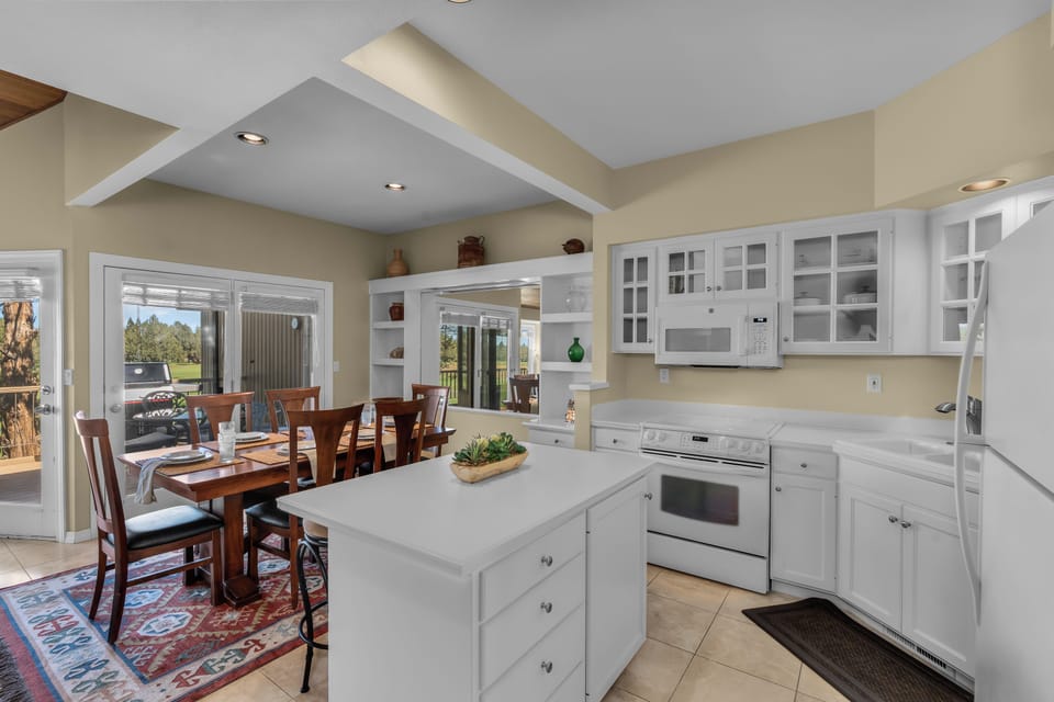 Picture yourself prepping meals in this bright, airy kitchen with its gleaming white cabinetry and generous island workspace. Glass-front cabinets and modern appliances blend seamlessly, while the open design flows into the dining area—perfect for gatherin