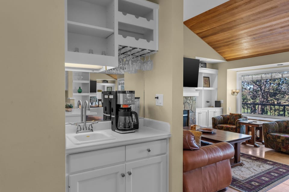 Enjoy your morning coffee at the dedicated beverage station with wine glass storage overhead, then settle into the inviting living room where rich leather seating and treetop views through expansive windows create your perfect retreat.