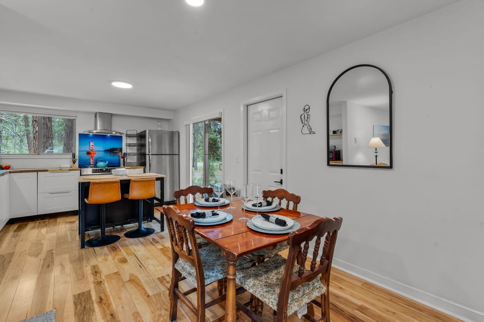 Gather around this cozy dining space where a beautifully set wooden table awaits your meals. The open-concept design flows into a modern kitchen with stainless steel appliances and island seating, perfect for your vacation cooking adventures.