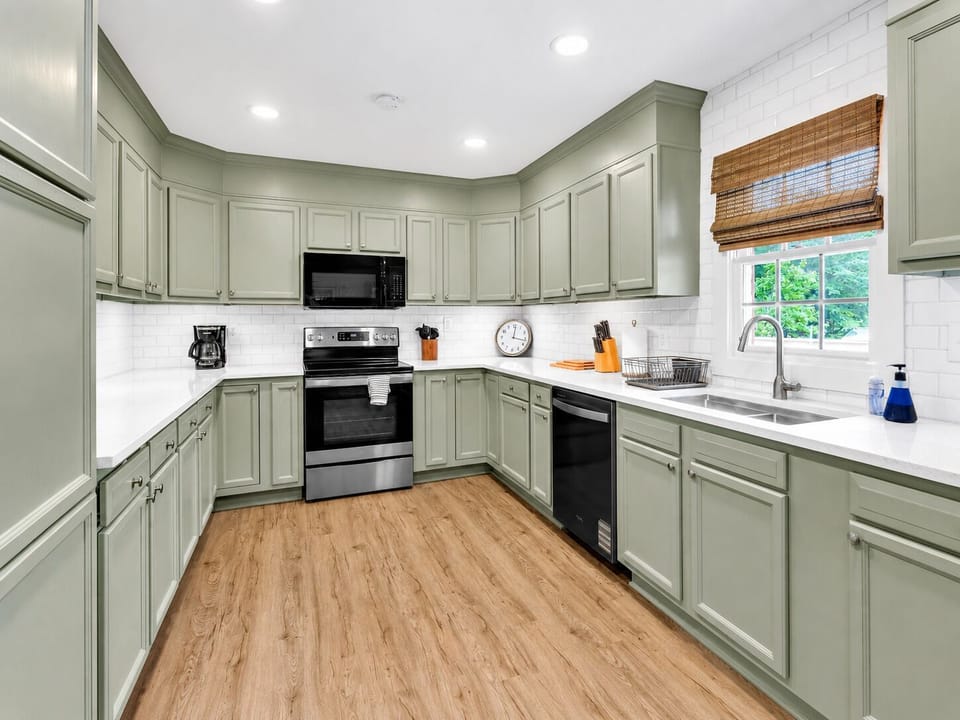 Fresh, fully equipped kitchen with sage green cabinetry, white counters, stainless appliances, and plenty of storage.