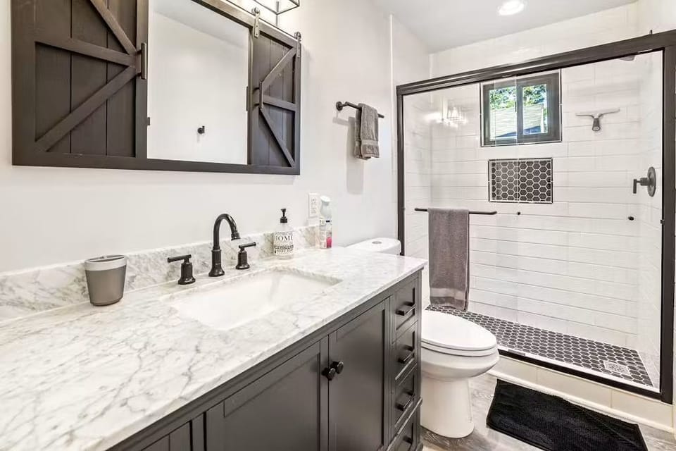 Bathroom featuring a dark vanity with marble-look counter and a subway tile shower.