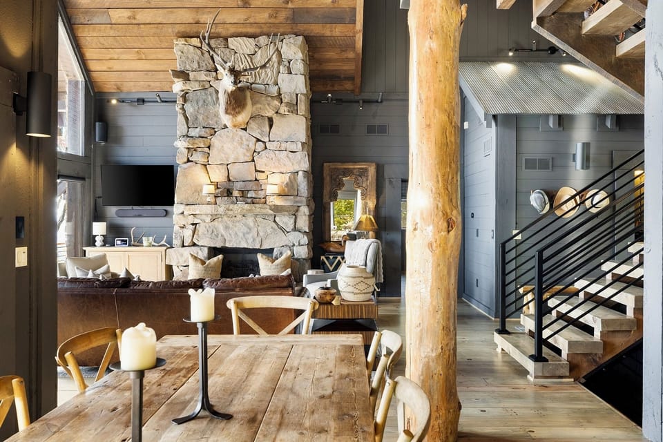 Linger at the table as candlelight meets the glow of the stone fireplace beyond. The great room unfolds in layers — dining, hearth, and a staircase into the beams.