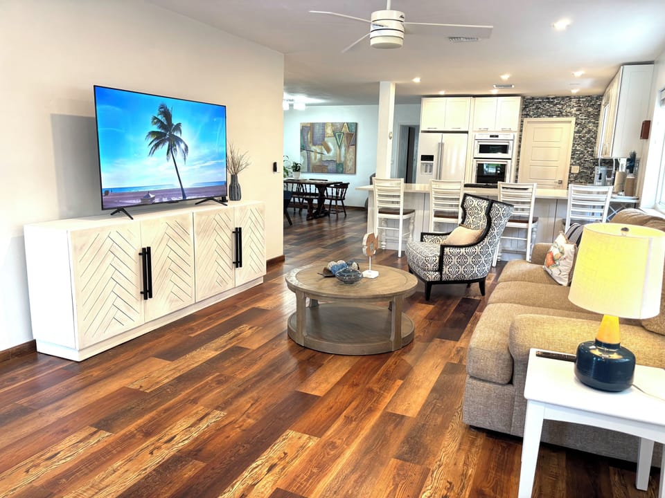 Bright open living area with large TV, cozy seating, and modern kitchen bar