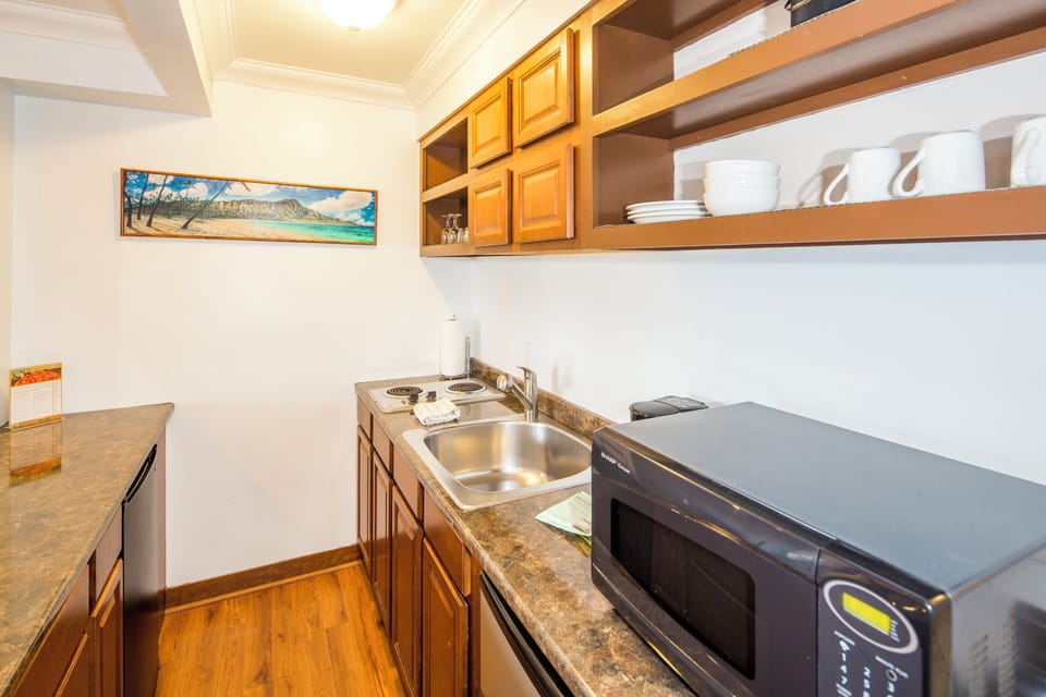 Your kitchenette features warm wood cabinetry, a stainless sink, electric burners, and a microwave, with dishware ready for easy meal prep during your stay.