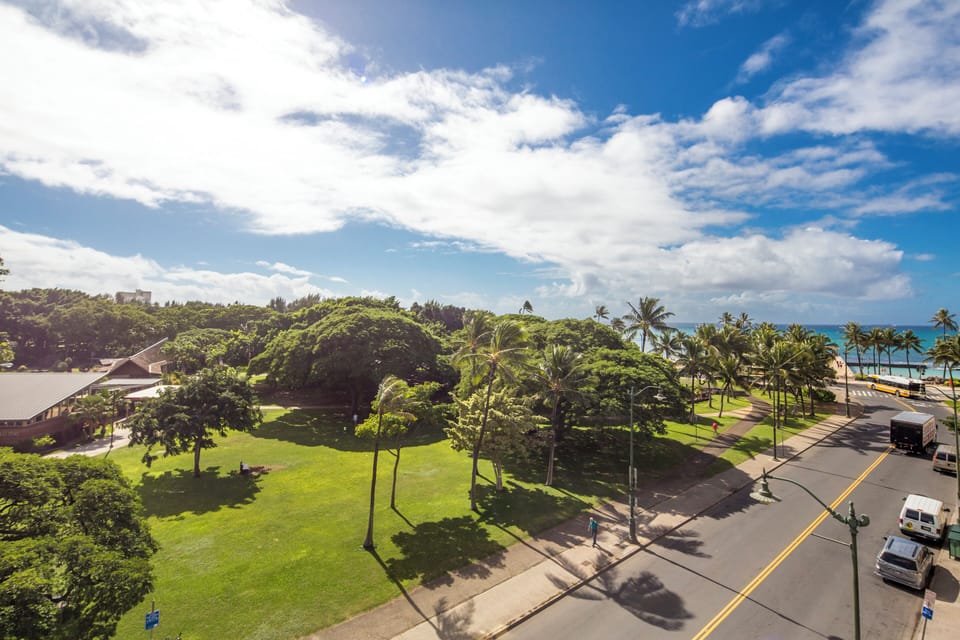 Beachfront property nestled between lush tropical landscaping and pristine ocean views, with palm trees lining the coastal road and expansive green spaces surrounding the main building.