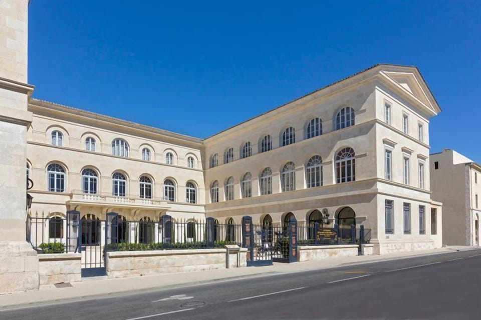 The historic stone facade of Le Grand Hôtel Dieu, a listed monument in the heart of Nîmes, steps from the Roman amphitheatre.